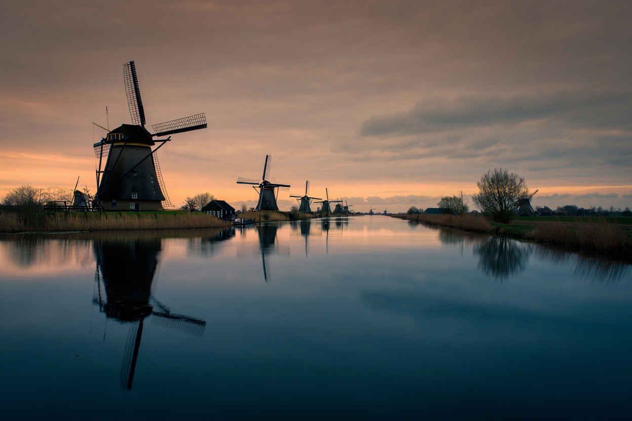 Rij historische windmolens bij Kinderdijk weerspiegeld in het rustige polderwater
